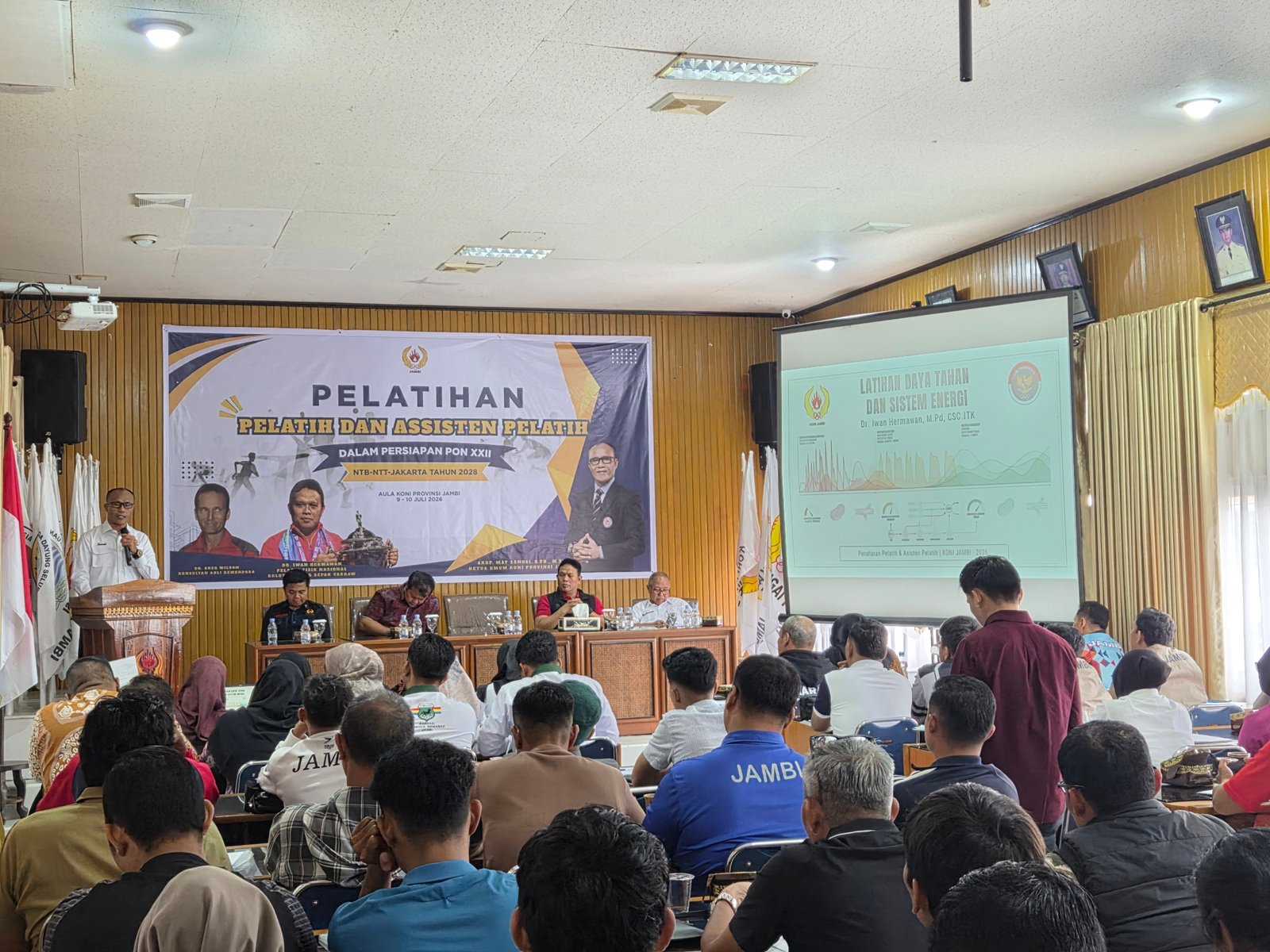 alt="Ketua Umum KONI Jambi AKBP Mat Sanusi berdiri memberikan pengarahan di depan puluhan pelatih 54 cabor"