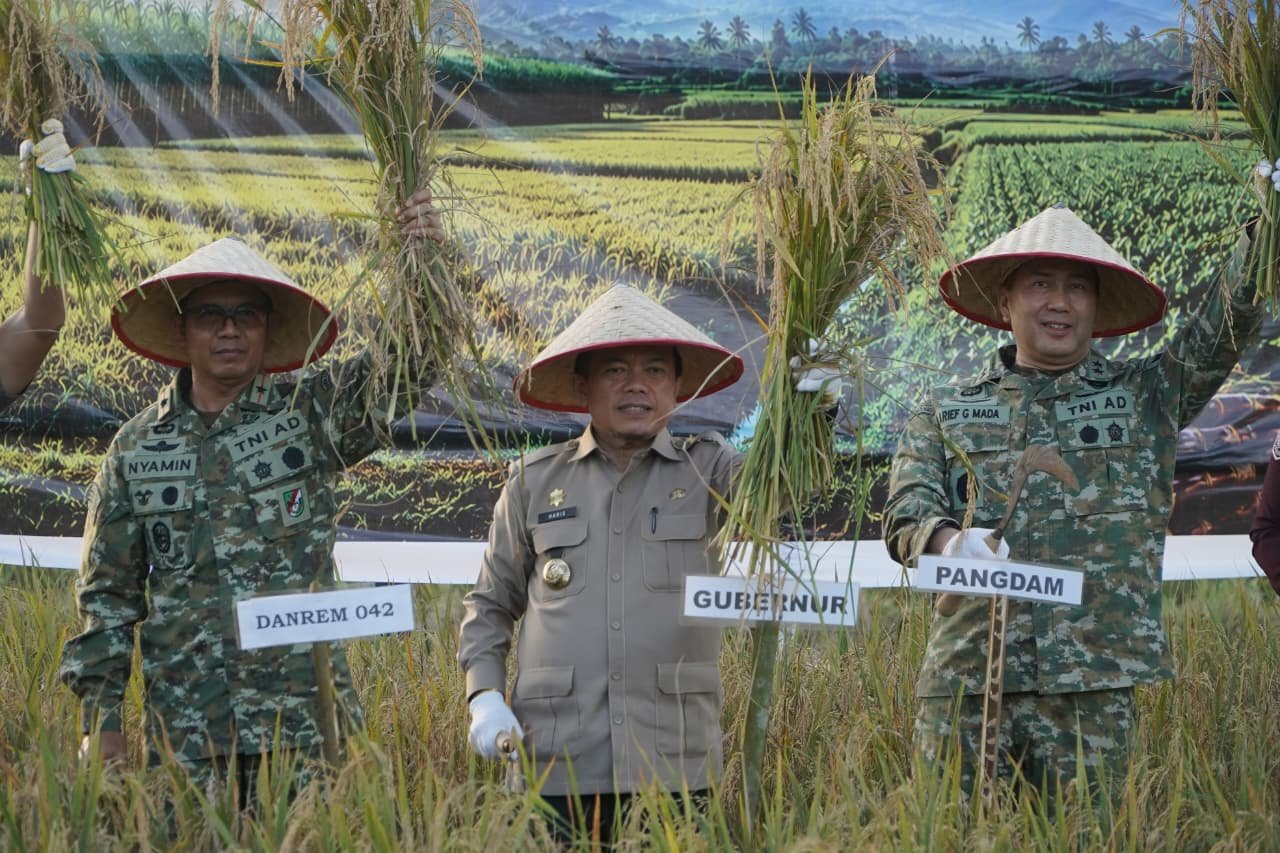 alt="Gubernur Jambi Al Haris memegang arit memotong padi bersama para pejabat militer di sawah Geragai"