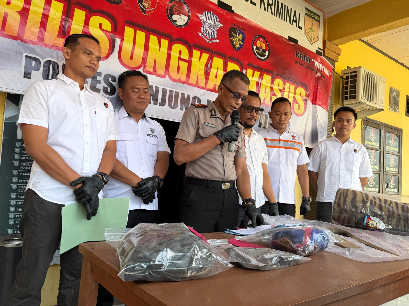 alt="Penyidik menunjukkan barang bukti parang dan pakaian korban pembunuhan sengketa lahan sawit"