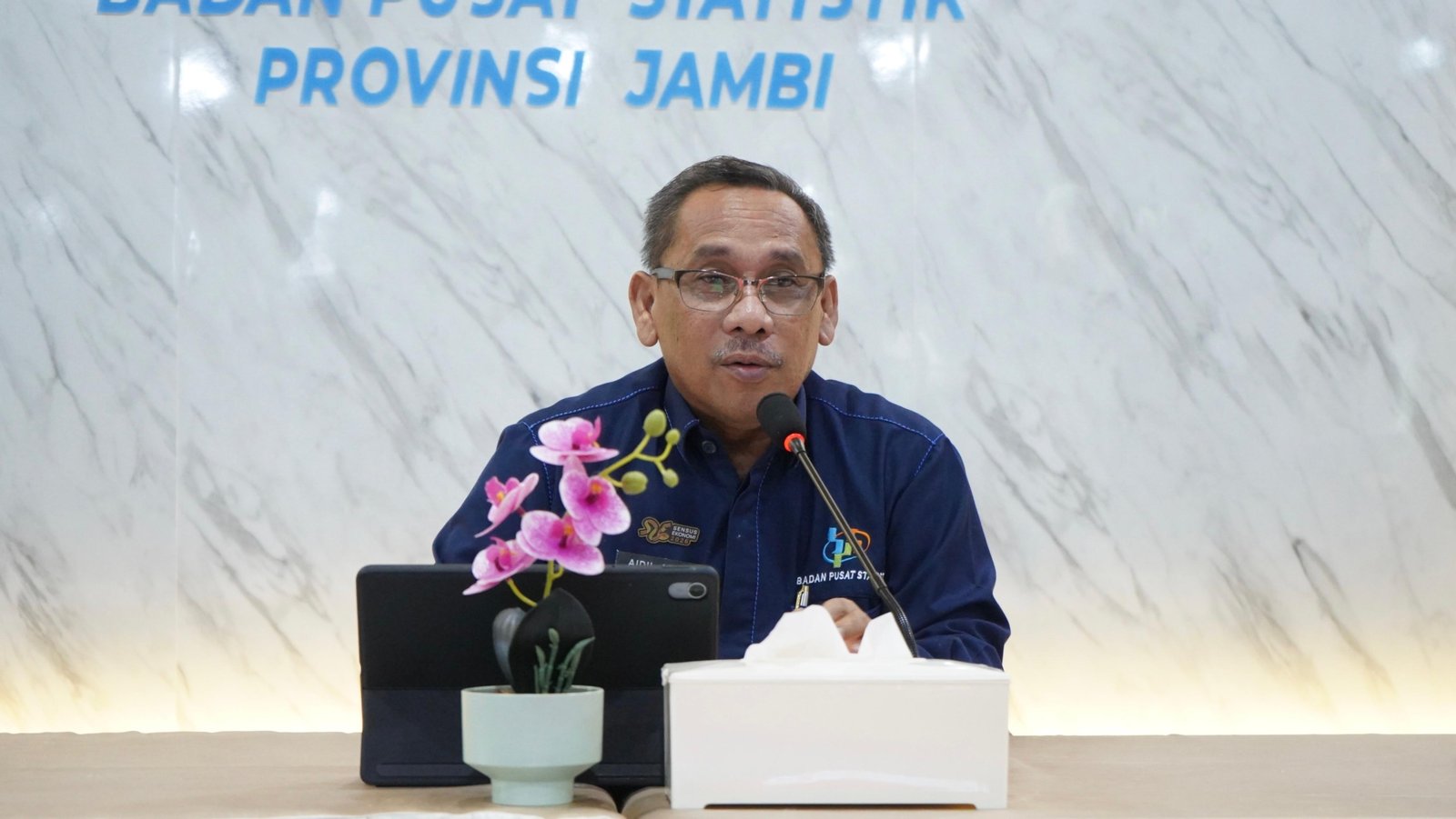 alt="Kepala BPS Provinsi Jambi Aidil Adha berdiri memaparkan data inflasi dan nilai tukar petani Juli 2026 di depan layar proyektor"
