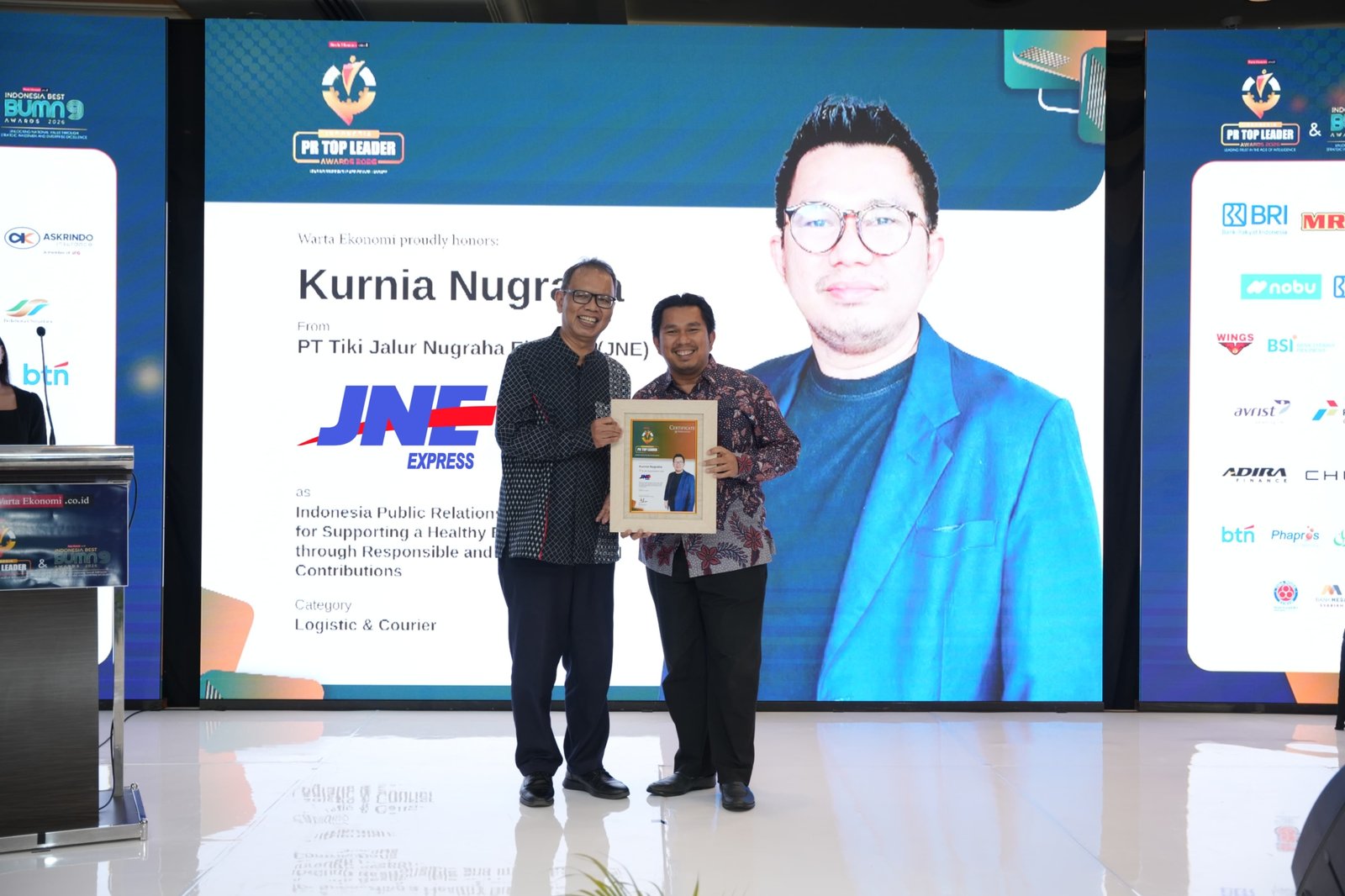 alt="Media Communication Head JNE Kurnia Nugraha memegang trofi penghargaan Indonesia Public Relations Top Leader 2026"