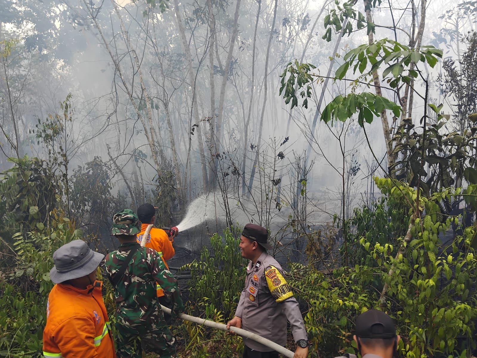 alt="Petugas gabungan Polres Muaro Jambi dan BPBD menyemprotkan air memadamkan karhutla di Jaluko"